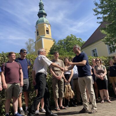 Superintendent Jan Mahling (Jan Malink) begrüßt Fabian Kaulfürst und die Teilnehmer des Sommerkurses für sorbische Sprache und Kultur (im Hintergrund Kirchturm der evangelischen Kirche Königswartha (obersorbisch Rakečanska cyrkej) © Sorbisches Institut (2022)