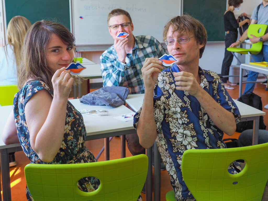 Drei lächelnde Kursteilnehmer:innen mit Magneten in Form eines Mundes in den sorbischen Farben (das Logo von "Sorbisch? Na klar.")