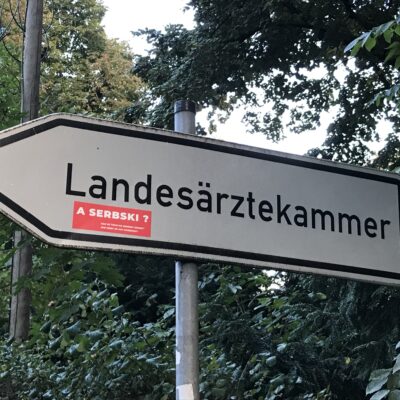 A serbski? [Und auf Sorbisch?] – lautet die Frage auf den roten Aufklebern, die seit einer Weile an vielen Stellen in Cottbus zu sehen sind, meistens auf Schildern und Plakaten mit einsprachiger deutscher Aufschrift. © Sorbisches Institut/Simon Blum (2022)