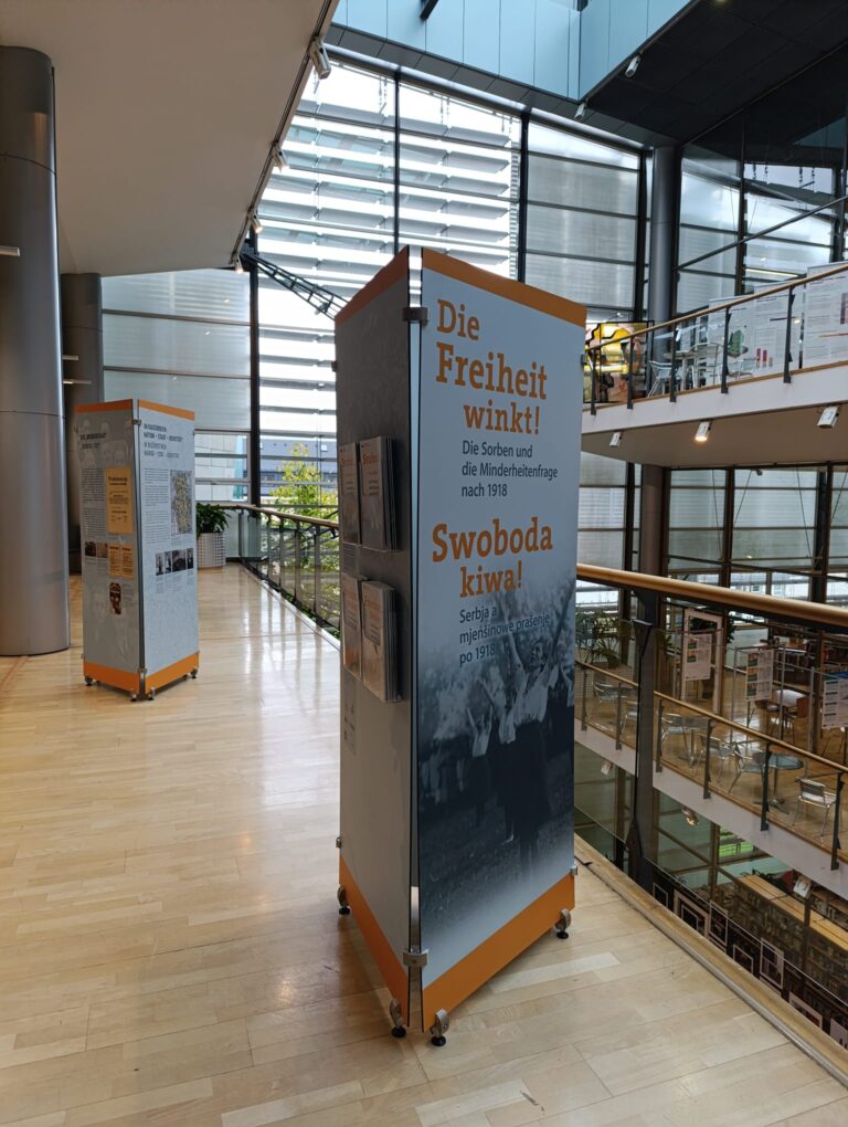 Wobraz pokazuje elementy pućowanskeje wustajeńcy ''Swoboda kiwa! - Serbja a mjeńšinowe prašenje po 1918'' we wědomostnej bibliotece w Liberecu. Nimo taflow srjedźa wobsahuja start wustajeńcy a spočatny motiw, kaž tež titul wustajeńcy. Na prawej kromje wobraza spóznaješ nimo toho tři dalše etaže wědomostneje biblioteki.