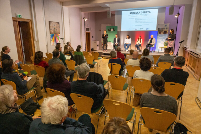 das Publikum von hinten mit Blick auf die Teilnehmenden der Debatte und auf eine Projektion des Beamers