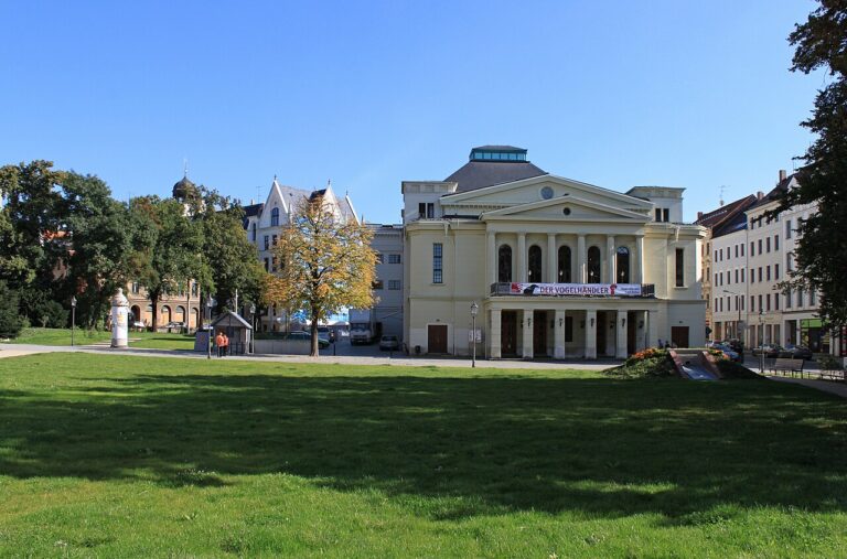 Blick über den Demianiplatz zum Gerhart Hauptmann-Theater Görlitz-Zittau in Görlitz, im Vordergrund Rasen, einige Bäume und angrenzende Bebauung, darüber blauer Himmel (Foto: LutzBruno, 2011)